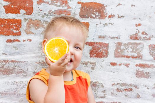 Portrait of child. Cute boy posing with an orange. The emotions of a child. Portrait of a boy against a brick wall.  