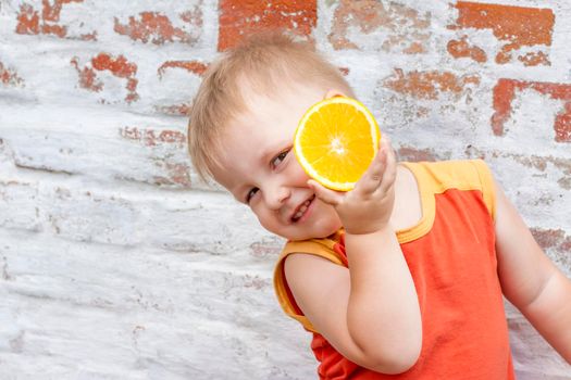 Portrait of child. Cute boy posing with an orange. The emotions of a child. Portrait of a boy against a brick wall.  