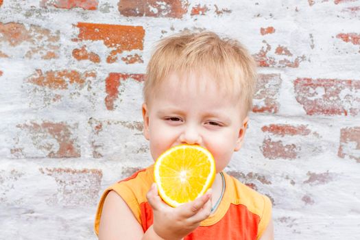 Portrait of child. Cute boy posing with an orange. The emotions of a child. Portrait of a boy against a brick wall. 