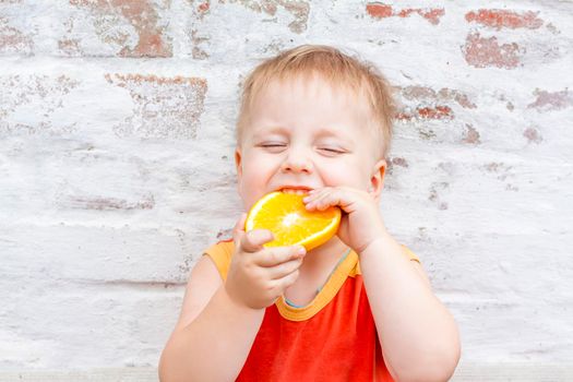 Portrait of child. Cute boy posing with an orange. The emotions of a child. Portrait of a boy against a brick wall.