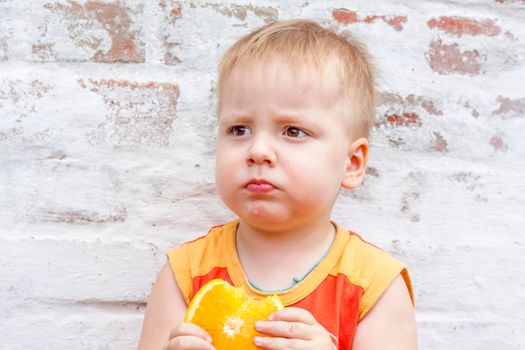 Portrait of child. Cute boy posing with an orange. The emotions of a child. Portrait of a boy against a brick wall. 