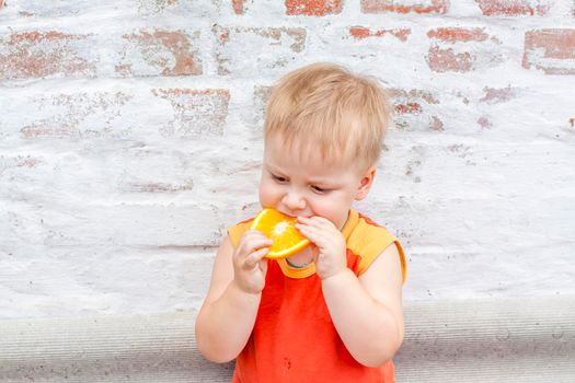 Portrait of child. Cute boy posing with an orange. The emotions of a child. Portrait of a boy against a brick wall. 