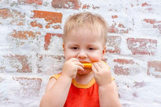 Portrait of child. Cute boy posing with an orange. The emotions of a child. Portrait of a boy against a brick wall.  