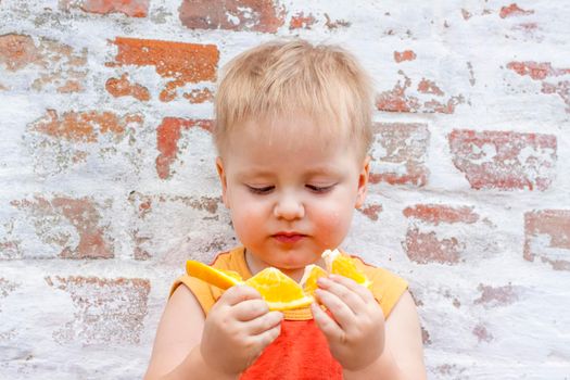 Portrait of child. Cute boy posing with an orange. The emotions of a child. Portrait of a boy against a brick wall.