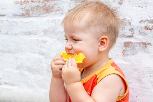 Portrait of child. Cute boy posing with an orange. The emotions of a child. Portrait of a boy against a brick wall.