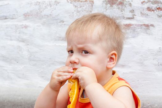 Portrait of child. Cute boy posing with an orange. The emotions of a child. Portrait of a boy against a brick wall. 