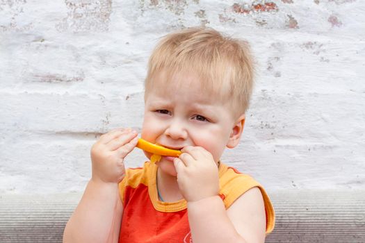 Portrait of child. Cute boy posing and eating a delicious orange. The emotions of a child. Portrait of child. Boy on the background of a brick wall.  