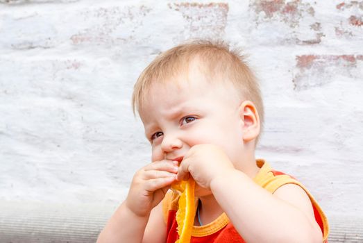 Portrait of child. Cute boy posing with an orange. The emotions of a child. Portrait of a boy against a brick wall.  