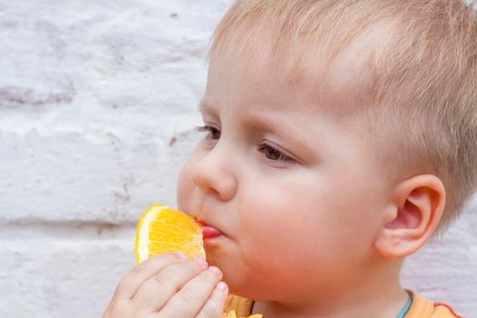 Portrait of child. Cute boy posing and eating a delicious orange. The emotions of a child. Portrait of child. Boy on the background of a brick wall.   