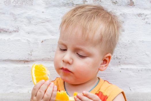 Portrait of child. Cute boy posing and eating a delicious orange. The emotions of a child. Portrait of child. Boy on the background of a brick wall.    