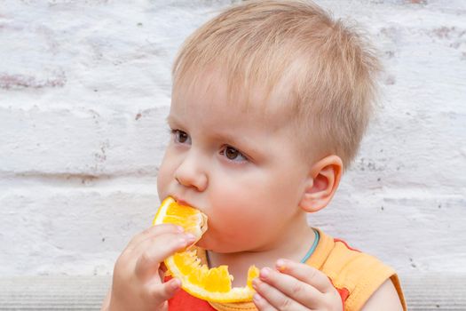 Portrait of child. Cute boy posing and eating a delicious orange. The emotions of a child. Portrait of child. Boy on the background of a brick wall.    