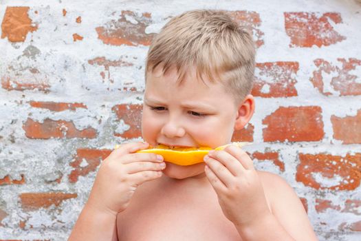 Portrait of child. Cute boy posing and eating a delicious orange. The emotions of a child. Portrait of child. Boy on the background of a brick wall.  