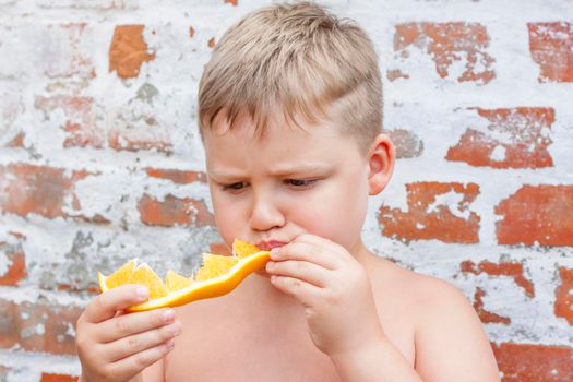 Portrait of child. Cute boy posing and eating a delicious orange. The emotions of a child. Portrait of child. Boy on the background of a brick wall.          