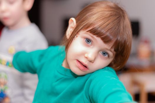 Portrait of a cute, brown-haired, blue-eyed, baby girl in green sweater in a kitchen