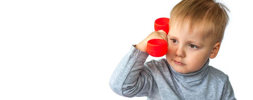 Portrait of a surprised cute little boy holding a red telephone receiver. The child is isolated on a white background. The concept of an advertising banner. Emergency call. Phone call. Phone in hand. 