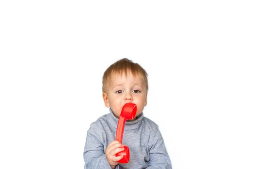 Portrait of a surprised cute little boy holding a red telephone receiver. The child is isolated on a white background. The concept of an advertising banner. Emergency call. Phone call. Phone in hand. 