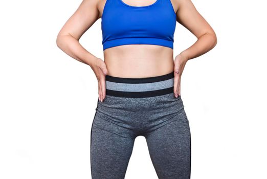 Fitness girl in a top and leggings points to her athletic figure. The Concept Of Weight Loss. Model on a white background. A slender Young Lady Holds her hands at her waist.