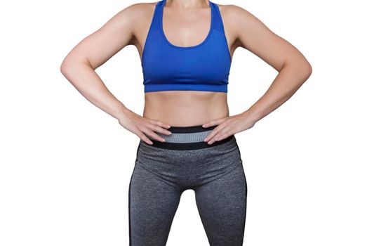 Fitness girl in a top and leggings points to her athletic figure. The Concept Of Weight Loss. Model on a white background. A slender Young Lady Holds her hands at her waist.