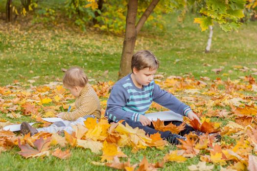 Children play in the autumn Park. The kids throw yellow leaves. Baby boy with a maple leaf. Autumn foliage. Family outdoor activities in the fall. Toddler or preschooler in the fall. 