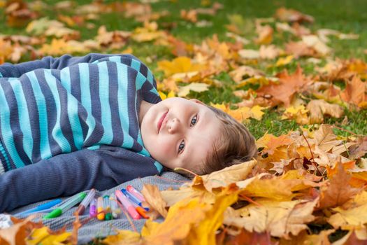 Children play in the autumn Park, around a lot of yellow leaves. The boy lies in the maple leaves. Autumn foliage. Family outdoor activities in the fall. Toddler or preschooler in the fall. 