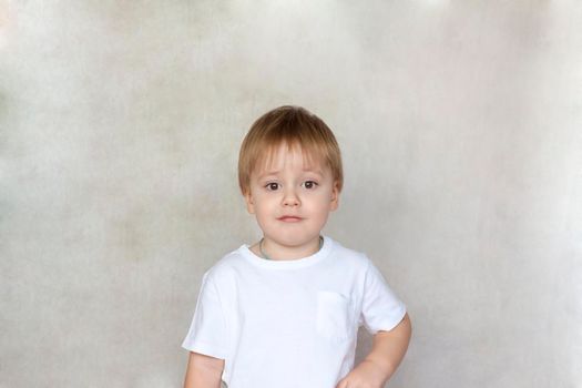 Portrait of a cute little boy in a white t-shirt. Children's emotions. Child on the background of the wall. Success, bright idea, creative ideas and concepts. The concept of an advertising banner. 