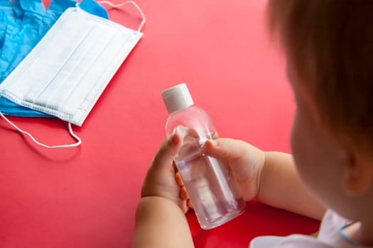 Medical mask with gloves and disinfectant in the child's hand on a red background. Mask for protection against influenza viruses, coronavirus, COVID-19.  Medical. 