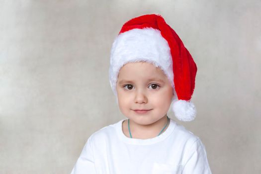 Portrait of a cute little boy in a white t-shirt and Santa Claus hat. Children's emotions. Christmas and new year. Success, bright idea, creative ideas and concepts. The concept of an advertising banner. 