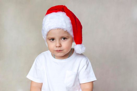 Portrait of a cute little boy in a white t-shirt and Santa Claus hat. Children's emotions. Christmas and new year. Success, bright idea, creative ideas and concepts. The concept of an advertising banner. 