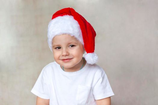 Portrait of a cute little boy in a white t-shirt and Santa Claus hat. Children's emotions. Christmas and new year. Success, bright idea, creative ideas and concepts. The concept of an advertising banner.