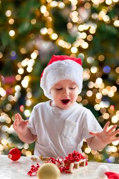 Child boy takes out of the box Christmas toys to dress up the tree. The Christmas tree is lit up and the baby looks at the Christmas toys with pleasure and joyful emotions. Christmas and new year.