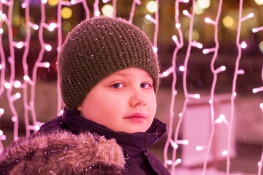 Portrait of a boy in the light of iridescent lights. Christmas in the city. illuminated decorations close-up. Photo