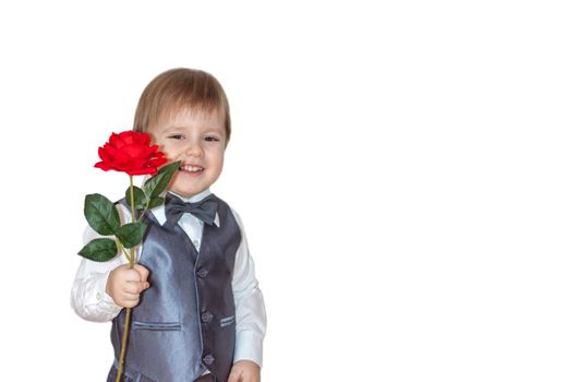 A little boy holds and hands over a red rose, the concept of the Valentine's Day theme. Portrait of a cute boy in a suit with a bow tie. Valentine's Day.