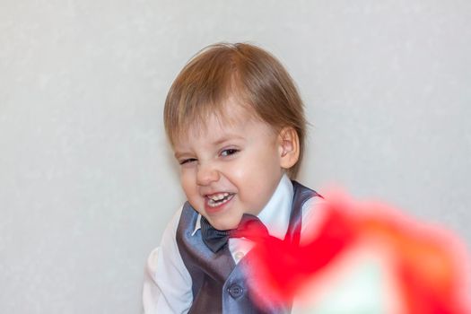 A little boy holds and hands over a red rose, the concept of the Valentine's Day theme. Portrait of a cute boy in a suit with a bow tie. Valentine's Day.