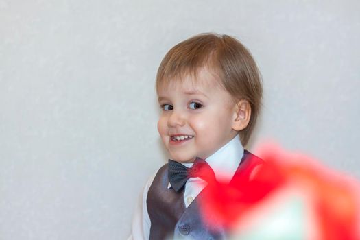 A little boy holds and hands over a red rose, the concept of the Valentine's Day theme. Portrait of a cute boy in a suit with a bow tie. Valentine's Day.