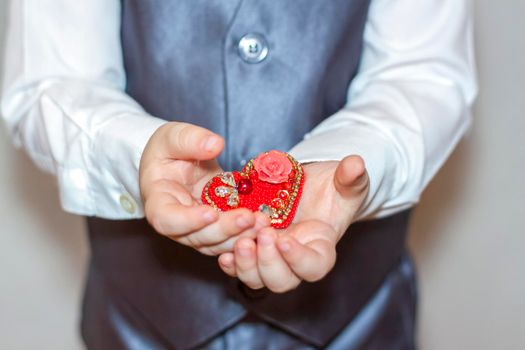 A little boy holds and hands a heart, the concept of the Valentine's Day theme. Hands of a boy in a suit close-up. Valentine's Day.