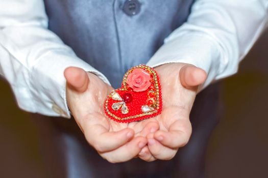 A little boy holds and hands a heart, the concept of the Valentine's Day theme. Hands of a boy in a suit close-up. Valentine's Day.