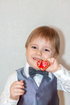 A little boy holds and hands a red heart, the concept of the Valentine's Day theme. Portrait of a cute boy in a suit with a bow tie. Valentine's Day.