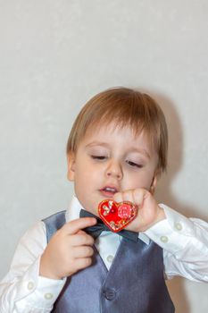 A little boy holds and hands a red heart, the concept of the Valentine's Day theme. Portrait of a cute boy in a suit with a bow tie. Valentine's Day.