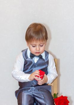 A little boy holds and hands over a red box, a Valentine's Day theme concept. Portrait of a cute boy in a suit with a bow tie. Valentine's Day.