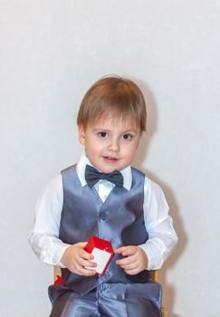 A little boy holds and hands over a red box, a Valentine's Day theme concept. Portrait of a cute boy in a suit with a bow tie. Valentine's Day. 