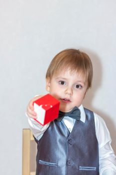 A little boy holds and hands over a red box, a Valentine's Day theme concept. Portrait of a cute boy in a suit with a bow tie. Valentine's Day.