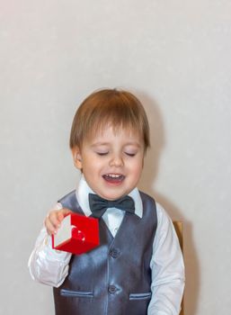 A little boy holds and hands over a red box, a Valentine's Day theme concept. Portrait of a cute boy in a suit with a bow tie. Valentine's Day.