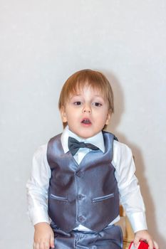 A little boy holds and hands over a red box, a Valentine's Day theme concept. Portrait of a cute boy in a suit with a bow tie. Valentine's Day.