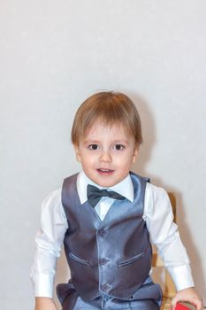 A little boy holds and hands over a red box, a Valentine's Day theme concept. Portrait of a cute boy in a suit with a bow tie. Valentine's Day. 