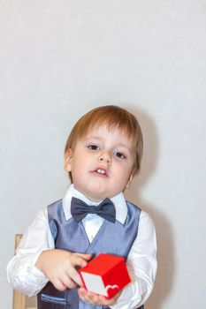 A little boy holds and hands over a red box, a Valentine's Day theme concept. Portrait of a cute boy in a suit with a bow tie. Valentine's Day.