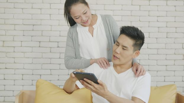 Asian family couple husband and wife work and using digital tablet. Cheerful loving couple smile shopping something online and watching social media together from home in living room,