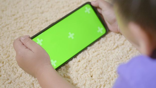 Asian kid boy preschool with gadget playing video games digital on mobile phone at home. Little child using and holding a smartphone green screen in hand, Technology generation concept