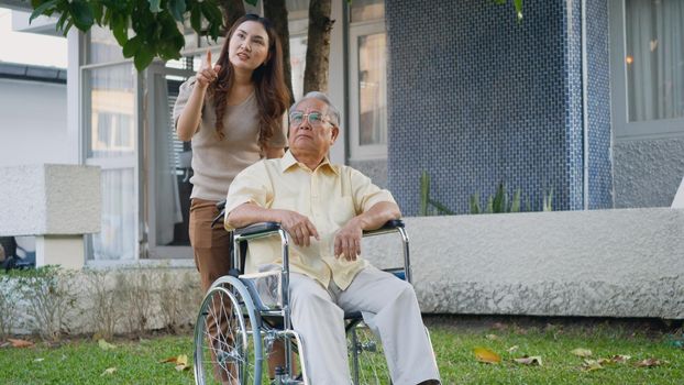 Disabled senior man on wheelchair with daughter, Happy Asian generation family having fun together outdoors backyard, Care helper young woman walking an elderly man smiling and laughed