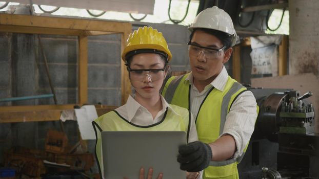 Asian professional mechanical engineer woman and operation man wearing uniform hardhat and goggles safety working on workshop metal lathe industrial manufacturing factory, Heavy industry lathe worker