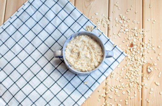 Fresh oatmeal porridge in a plate on a beautiful napkin and on a wooden table. A fresh and healthy breakfast.